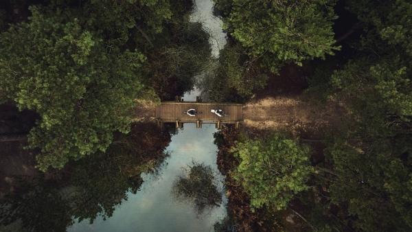 Vue du ciel - Deux cyclistes traversent un pont dans les bois