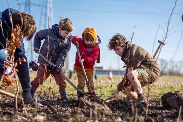 Trois enfants, pelle à la main, font du jardinage avec un adulte